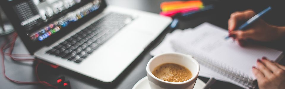 Macbook mit Kaffee, Händen und Schreibblock